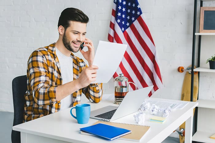 man talking at cellphone sitting in a desk american flag